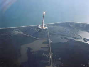 Space shuttle Challenger rising on a column of smoke over the Florida coast, seen from above