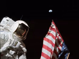 Harrison Schmitt beside the U.S. flag on the Moon, with Earth small in the black sky