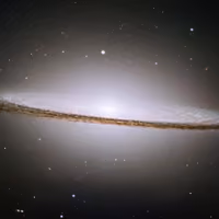 Sombrero galaxy seen edge-on, a bright white core crossed by a dark band of dust