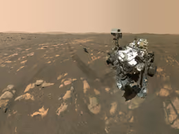 Perseverance rover beside the small Ingenuity helicopter on reddish Martian ground