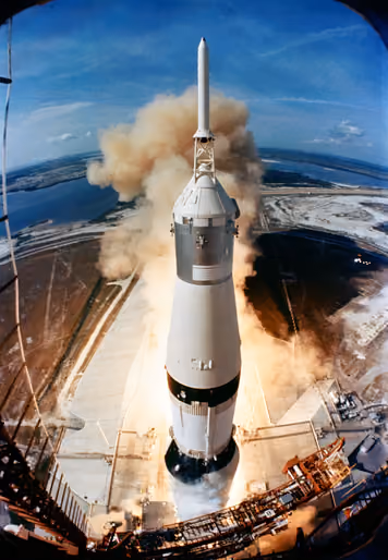 Saturn V rocket lifting off beside its launch tower in a cloud of flame and smoke