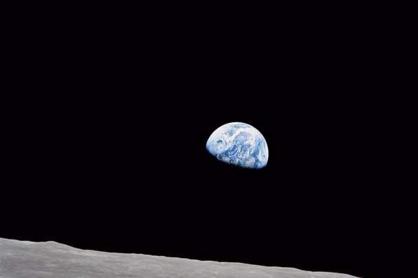 Earth, half in shadow, rising above the grey horizon of the Moon