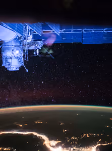 City lights on the night side of Earth under thousands of stars, with part of the space station