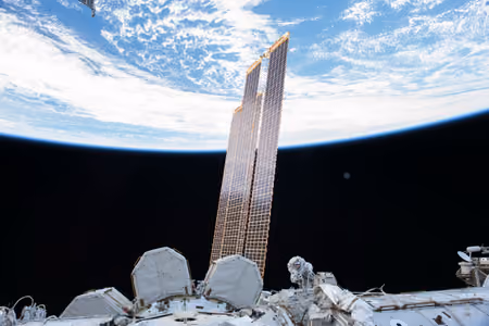 Astronaut Randy Bresnik dwarfed by the space station's huge solar arrays, with Earth behind