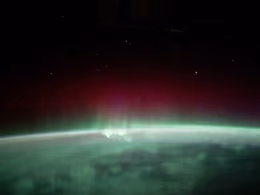 Green and red aurora over the dark curve of the Earth, seen from orbit