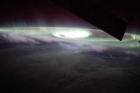 Green aurora australis swirling above clouds over the Pacific, seen from orbit