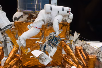 Astronaut in a white spacesuit working on the gold-foil body of the Hubble Space Telescope